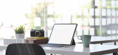 Arka planda güneş ışığı olan dijital tablet, kamera ve ofis malzemeleriyle dolu rahat bir ofis odası. 