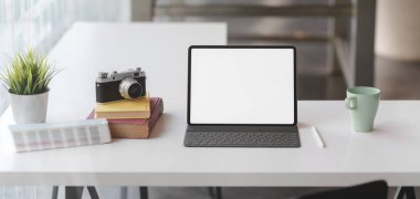 Beyaz masa üzerinde boş tablet, kamera ve ofis malzemeleriyle modern ofis odasının yakın görüntüsü.