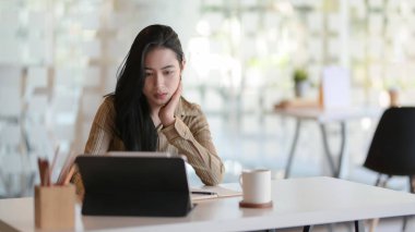 Modern ofis odasındaki tabletle projesinde çalışan genç ve güzel bir iş kadınının görüntüsü. 