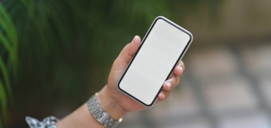 Profesyonel iş adamının arka planda bulanık bahçeli boş ekran akıllı telefonu tutarken çekilmiş görüntüsü.