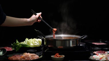 Shabu-Shabu 'yu taze et, deniz yemeği ve siyah arka planda sebzelerle sıcak bir tencerede yiyen bir kadının görüntüsü. Japon mutfağı.
