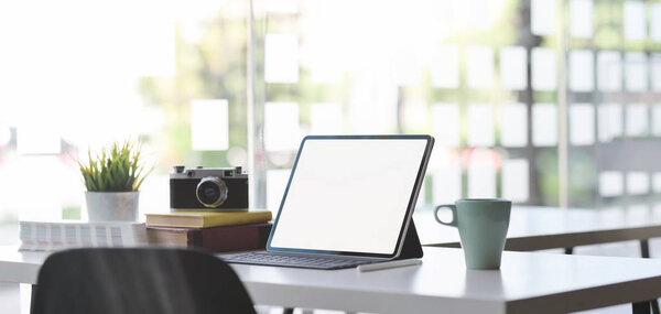 Удобная офисная комната с макетом цифрового планшета, фотоаппарата и офисных принадлежностей с солнечным светом в фоновом режиме
 