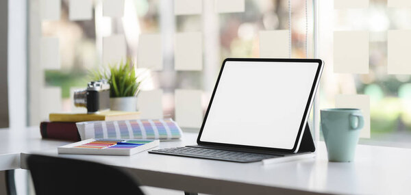 Cropped shot of modern designer workplace with blank screen tablet on white wooden table with office supplies 