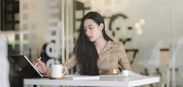 Porträt einer jungen schönen asiatischen Designerin, die an ihrem Projekt arbeitet, während sie ein digitales Tablet am modernen Arbeitsplatz benutzt — Stockfoto