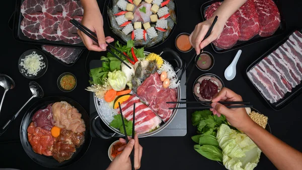 Shabu-Shabu 'yu taze et, deniz ürünü ve siyah arka planda sebzelerle sıcak tencerede yiyen insanların en iyi görüntüsü. Japon mutfağı.