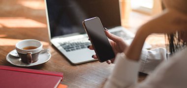 İş kadınının rahat çalışma alanında projesinde çalışırken akıllı telefonunu kullanmasının yakın plan görüntüsü 