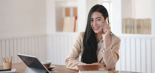 Porträt einer jungen Geschäftsfrau, die mit einem Kunden telefoniert und in die Kamera lächelt — Stockfoto