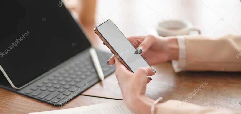 Close-up view of young businesswoman using her smartphone while working on her project in comfortable workspace 