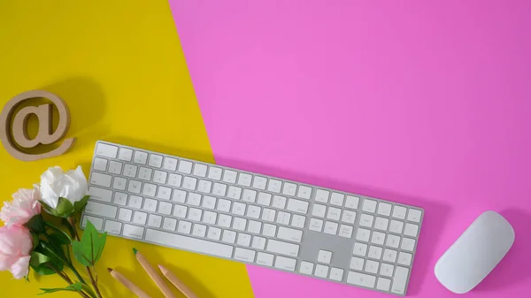 Vista superior do espaço de trabalho colorido com teclado e material de escritório em fundo de mesa amarelo e rosa com espaço de cópia — Fotografia de Stock