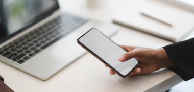 Bulanık ofis arka planında dizüstü bilgisayarla çalışırken akıllı telefon kullanan bir iş kadını görüntüsü. 
