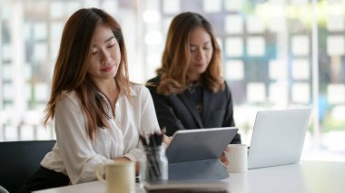 Modern ofis odasında proje üzerinde çalışan iki profesyonel iş kadını. 