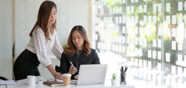 Modern ofis odasında proje üzerinde çalışan iki profesyonel iş kadını. 