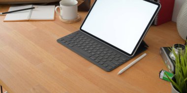 Boş ekran dijital tableti ve ahşap masa üzerindeki ofis malzemeleriyle rahat bir iş yeri görüntüsü. 