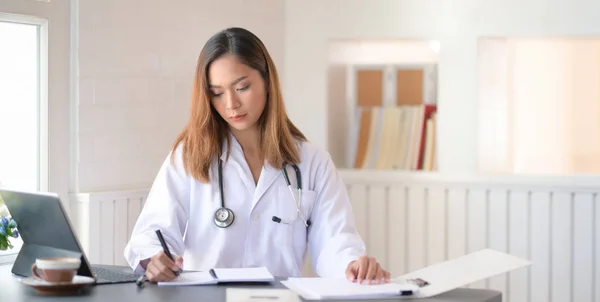 Veduta ravvicinata del giovane medico donna che scrive cartelle cliniche con — Foto Stock