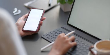 Ofis odasında boş ekran akıllı telefon kullanırken dijital tablete yazı yazan genç iş kadınının yakın plan görüntüsü 