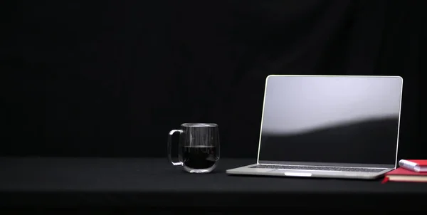 Темное трехмерное рабочее место с открытым ноутбуком, чашкой кофе и ноутбуком на черном столе — стоковое фото