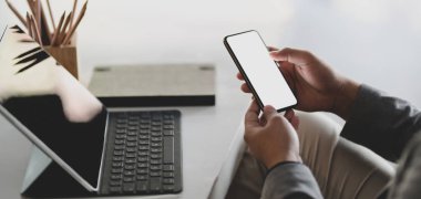 Ofis odasında çalışırken genç işadamının boş ekran akıllı telefonu kullanırken görüntüsü kesilmiş. 