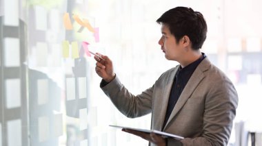 Genç tutkulu işadamı fikirleri modern ofis odasındaki yapışkan nottan topluyor. 