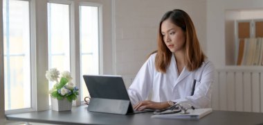 Hastane ofisinde tabletle tıbbi kayıtlar üzerinde çalışan genç bir doktor.