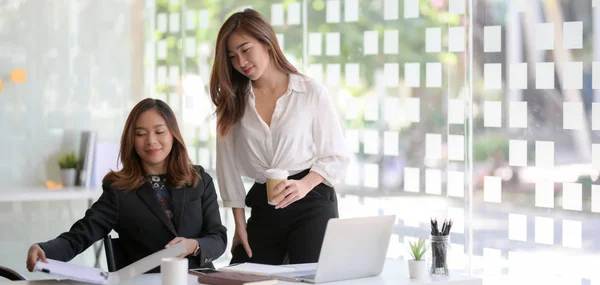 Două tinere femei de afaceri profesionale care lucrează la proiectul lor împreună cu laptopul în sala de birouri modernă — Fotografie, imagine de stoc