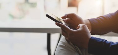 Proje üzerinde çalışırken akıllı telefon kullanan genç iş adamının görüntüsü. 