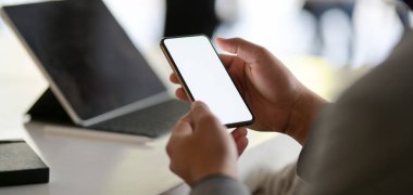 Modern ofis odasındaki boş ekran akıllı telefona bakan genç iş adamının kırpılmış görüntüsü. 