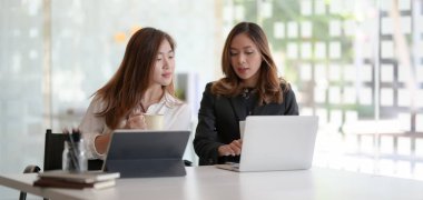 Modern ofis odasında proje planına danışmanlık yapan iki genç profesyonel iş kadını 