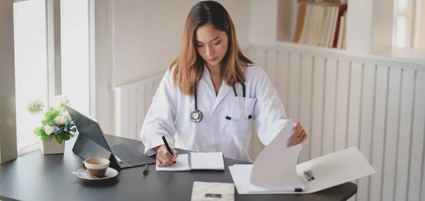 Giovane dottoressa che lavora su cartelle cliniche e documenti nella sua stanza d'ufficio — Foto Stock