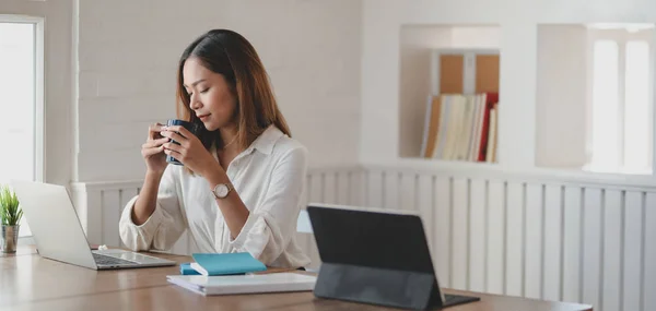 Обрізаний знімок молодої бізнес-леді, яка працює над своїм проектом і п'є чашку кави в сучасній офісній кімнаті — стокове фото