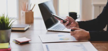 İş yerinde akıllı telefon kullanırken genç bir iş kadınının projesi üzerinde çalışırken görüntüsü kesilmiş. 