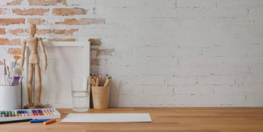 Boya aletleri ve ofis malzemeleriyle ahşap masa ve tuğla duvar arka planında özel tasarım işyeri. 