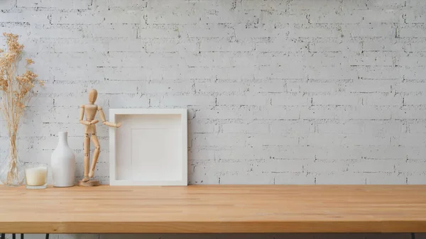 Vista de cerca del espacio de trabajo moderno con figura de madera, marco y decoraciones en mesa de madera con fondo de pared de ladrillo blanco —  Fotos de Stock