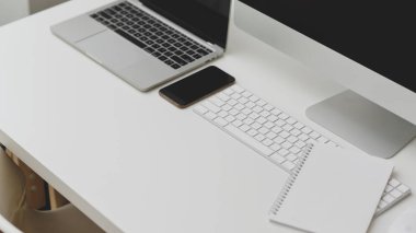 Ofis malzemeleri, laptop, bilgisayar ve akıllı telefonlar beyaz masada.  