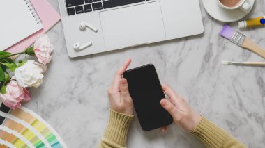 Üst görünüm modern çalışma alanında dizüstü bilgisayarı, kablosuz kulaklığı ve mermer masadaki boya aletleriyle akıllı telefon tutuyor.