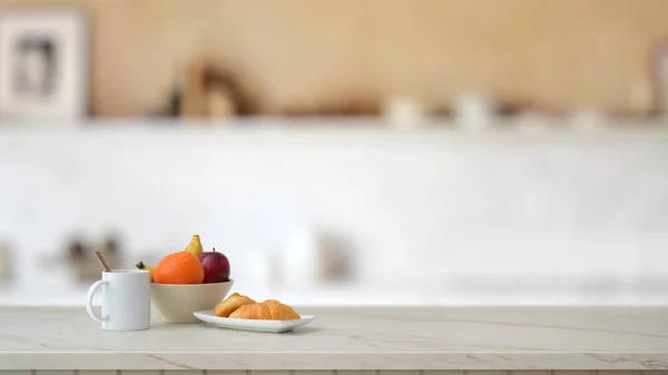 Vista de perto da fruteira, xícara de café e croissant na mesa de mármore com sala de cozinha borrada — Fotografia de Stock