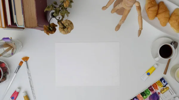 Vista superior do espaço de trabalho com papel de esboço, ferramentas de pintura, xícara de café e material de escritório na mesa branca — Fotografia de Stock