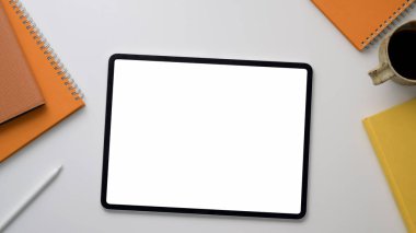 Tablet, ofis malzemeleri ve beyaz masa üzerinde kahve fincanı olan iş yeri manzarası.
