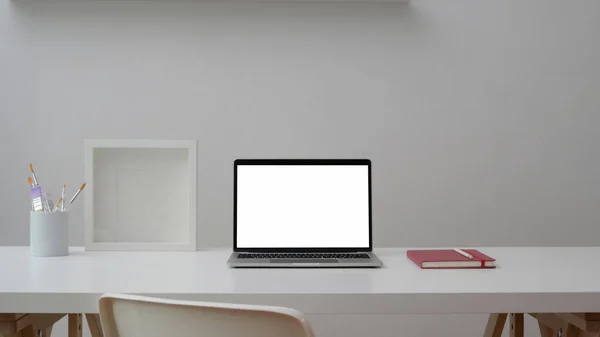 Oříznutý záběr pracovního prostoru s otevřeným prázdným obrazovkou notebookem, rámečkem, notebookem a štětcem na bílém stole s bílou stěnou — Stock fotografie