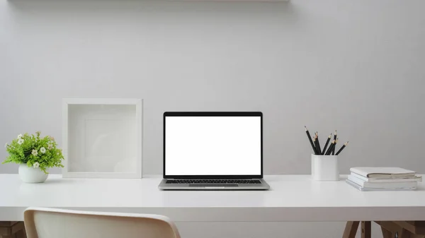 Primer plano del espacio de trabajo con ordenador portátil de pantalla en blanco, marco, papelería y macetas de árbol en la mesa blanca con pared blanca —  Fotos de Stock