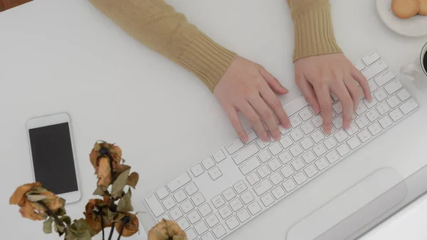 Top view női gépelés a számítógépen a modern munkaterület cookie-k, okostelefon és száraz rózsák fehér íróasztal háttér — Stock Fotó