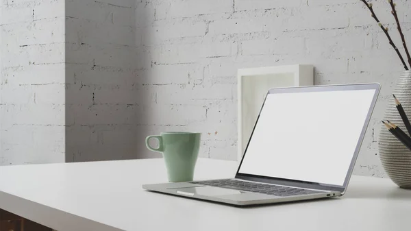 Vue rapprochée de l'espace de travail avec ordinateur portable à écran vierge, tasse à café et décorations sur withe bureau avec mur de briques — Photo