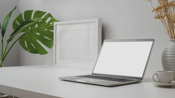 Närbild av arbetsyta med tom skärm laptop, mock up ram och keramik vas på withe skrivbord med vit vägg — Stockfoto