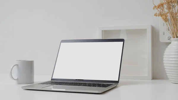 Cropped shot of workspace with blank screen laptop, mock up frame and ceramic vase on withe desk with white wall — 스톡 사진