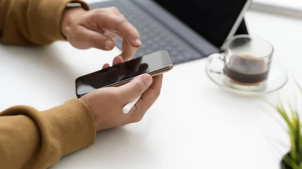 Captura recortada de mensajes de texto en el teléfono inteligente mientras se trabaja en un espacio de trabajo simple con la tableta y la taza de café — Foto de Stock