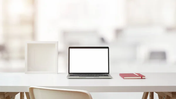Vista de cerca del espacio de trabajo con el ordenador portátil de pantalla en blanco abierto, marco y portátil en la mesa blanca con sala de oficina borrosa — Foto de Stock