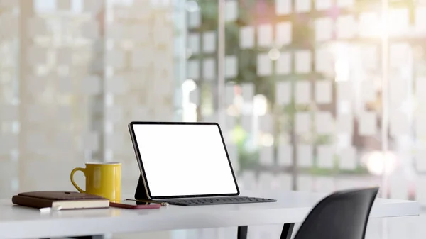 Afgeknipte opname van de werkruimte met blanco tablet, kantoorbenodigdheden en koffiebeker op witte tafel met wazig kantoor — Stockfoto
