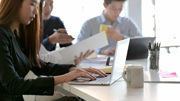 Tiro cortado de negócios digitando no laptop enquanto se situa na sala de reuniões com colegas de trabalho e material de escritório — Fotografia de Stock