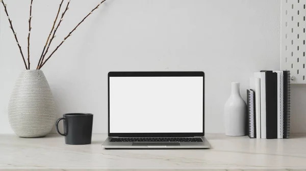 Cropped shot of workplace with blank screen laptop, decorations, books and coffee up on marble desk with white wall — 스톡 사진