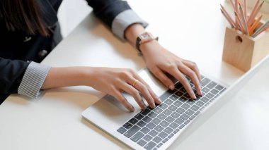 İş kadınının basit çalışma alanındaki bilgisayarında ofis malzemeleriyle yazı yazarken görüntüsü.