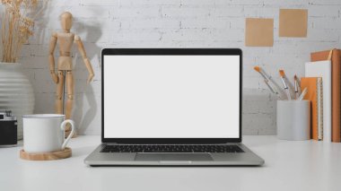 Boş ekran dizüstü bilgisayarı, ahşap figür, boya fırçası ve beyaz masadaki beyaz tuğlalı kahve fincanını kapat. 